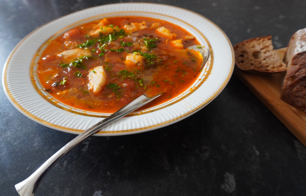 Moroccan fish soup in serving plate with pieces of fish garnished with parsley angle view