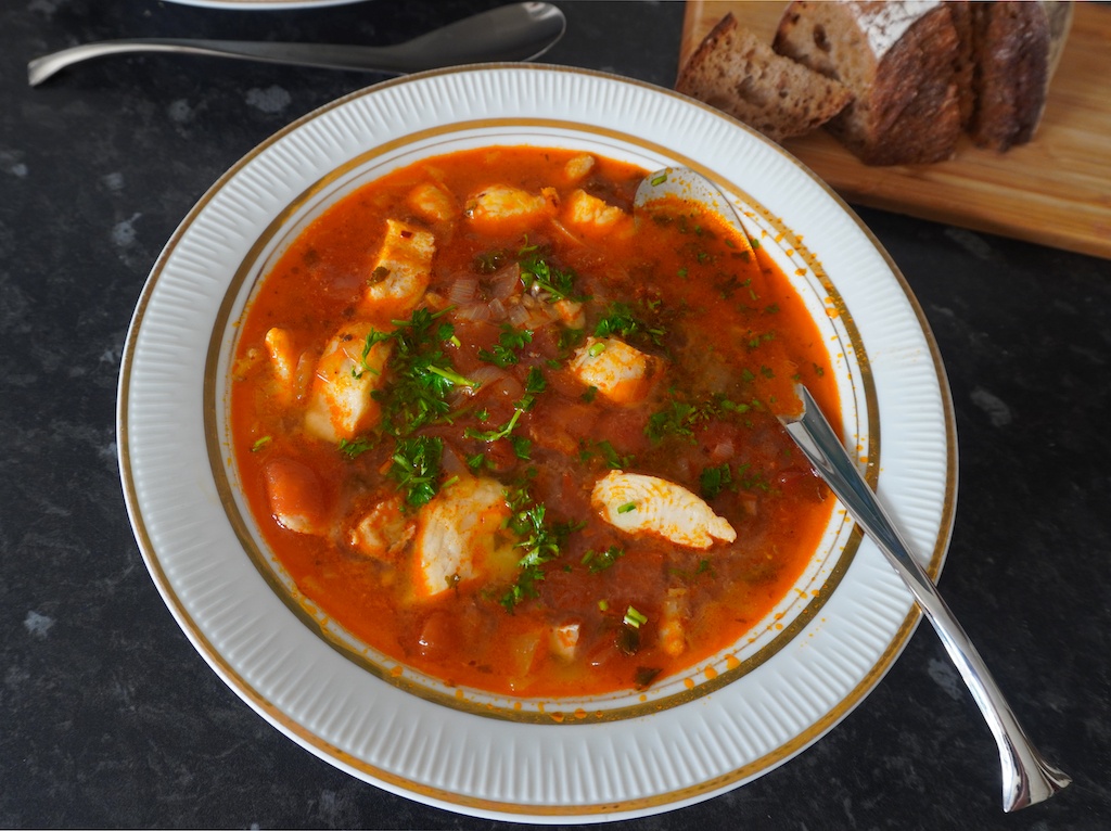 Moroccan fish soup in serving plate with pieces of fish garnished with parsley on the side bread on chopping board