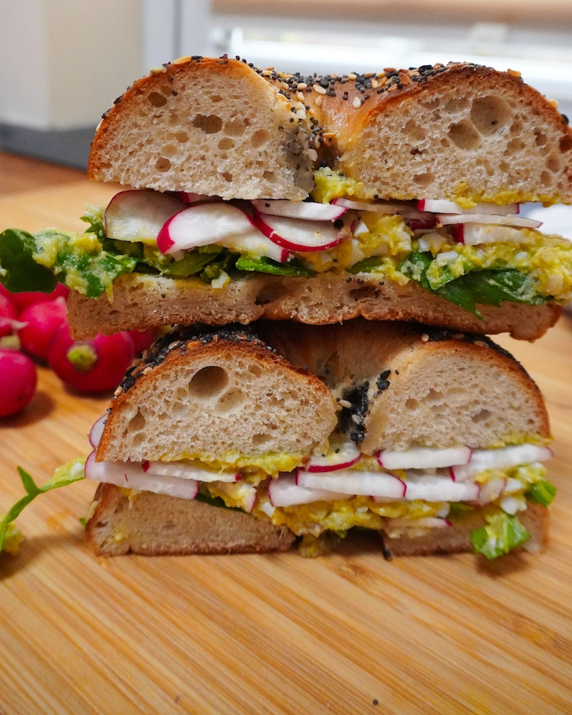 avocado bagel sandwich cut in half and placed one on the other - radishes, avocado spread and lettuce inside