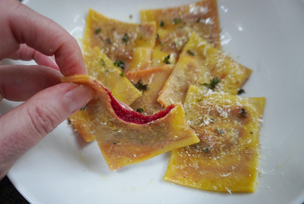 beetroot ravioli - ravioli with beetroot filling in pasta bowl, one raviolo in hand with a corner bitten out