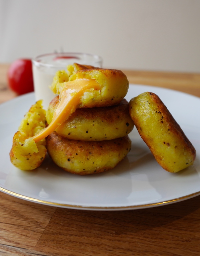 cheese stuffed potatoes in serving plate stacked up on each other one piece cut open with cheese melting out close up