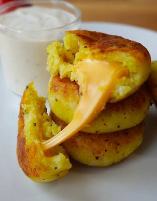 cheese stuffed potatoes in serving plate stacked up on each other one piece cut open with cheese melting out close view on cheese