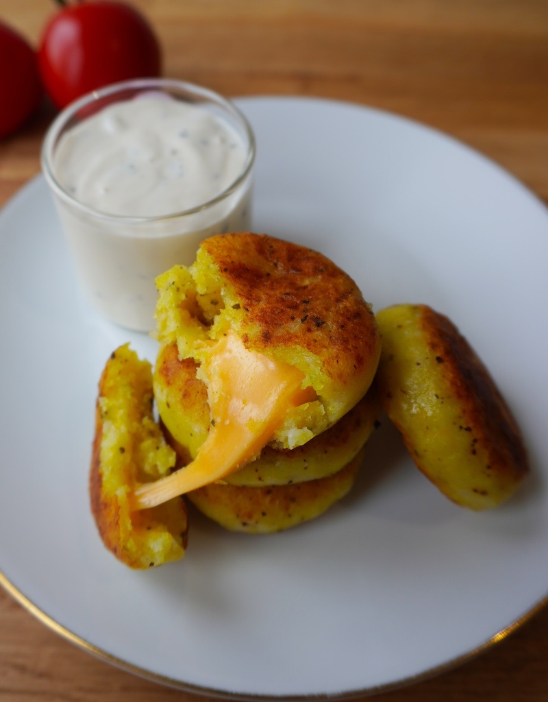 cheese stuffed potatoes in serving plate stacked up on each other one piece cut open with cheese melting out flat lay