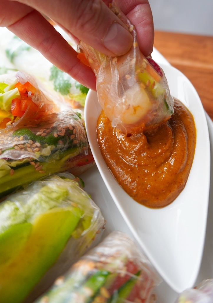 close up on hand dipping spring roll in peanut butter sauce spring rolls around the saucer