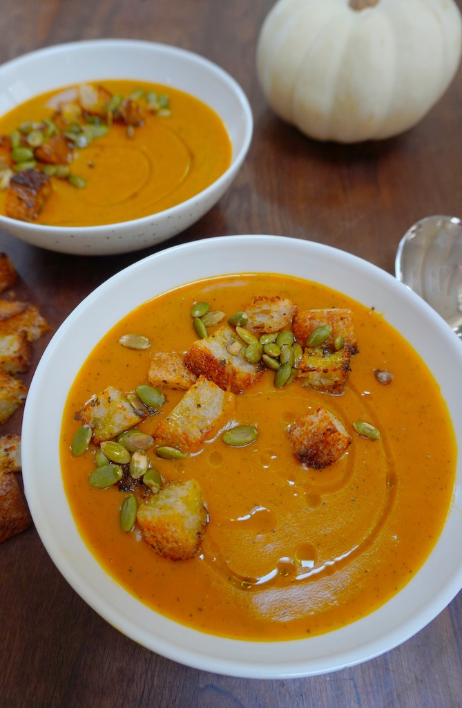 close up on pumpkin soup in two serving bowls pumpkin croutons and a spoon at the table