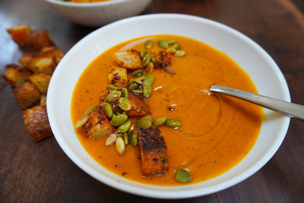 comforting pumpkin soup in a bowl with a spoon, croutons and pumpkin seeds on