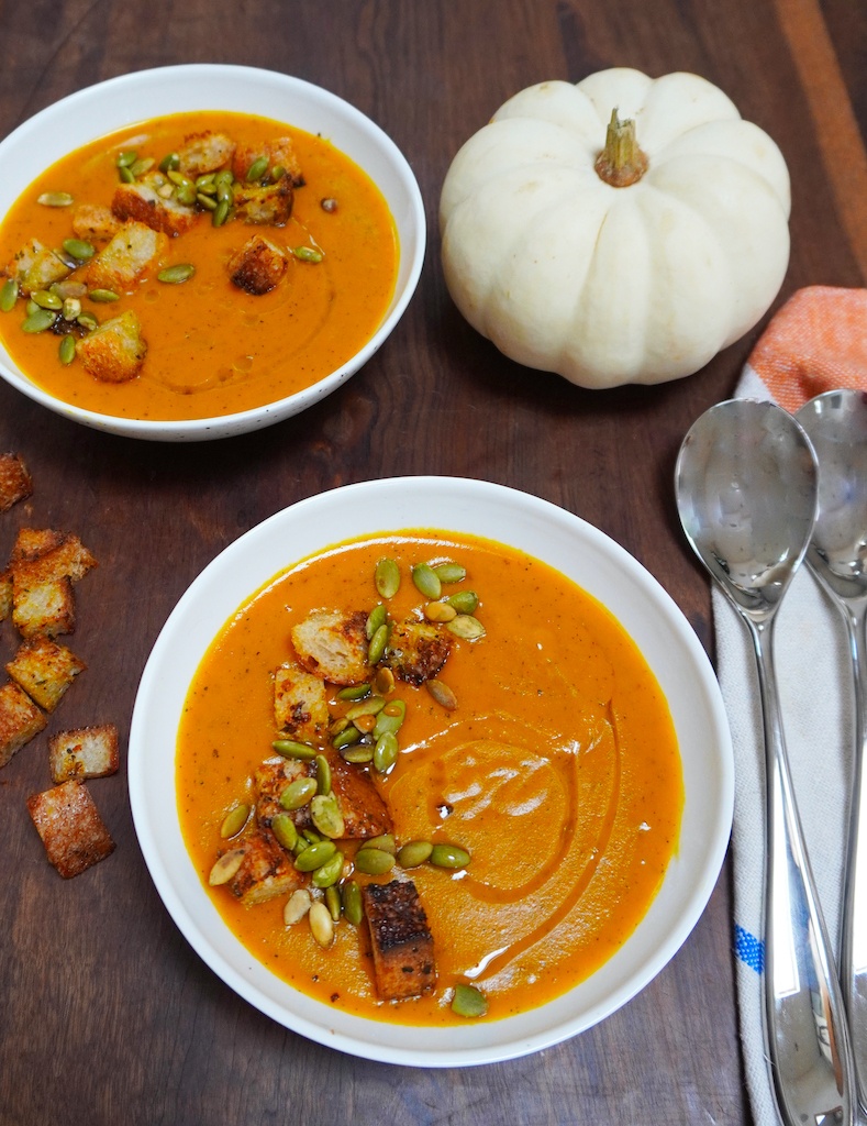 comforting pumpkin soup in two bowls and a pumpkin on the table spoons at the side