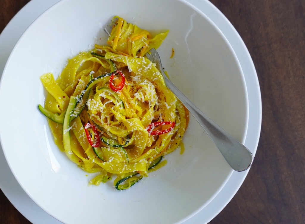 courgette pasta in pasta bowl hand-made pasta with spiralized yellow and green courgette and chilli sprinkled with grated parmesan flat lay close view