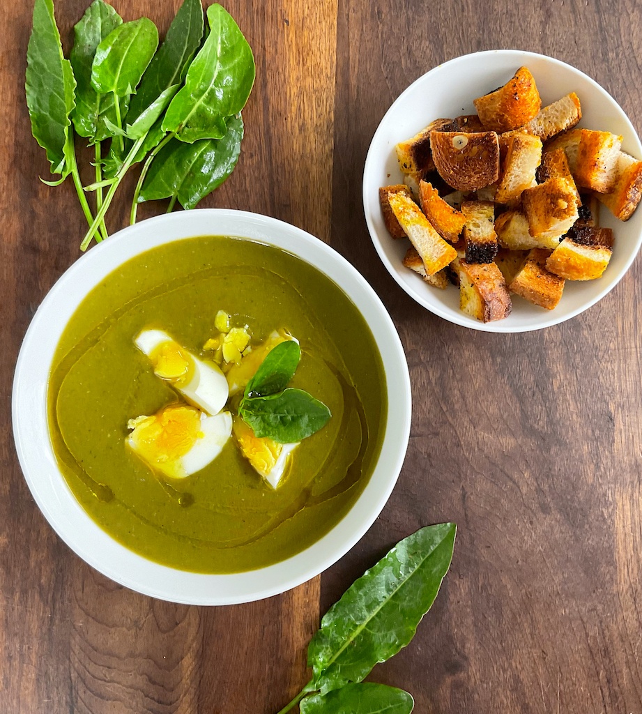 creamy sorrel soup in a serving bowl garnished with egg, croutons in a bowl flat lay