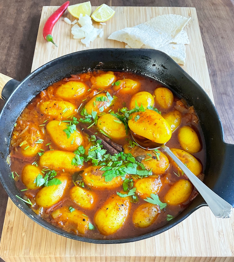 dum aloo or dum alu in a cast iron skillet on a wooden board with a spoon in