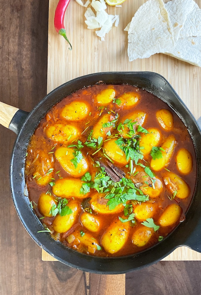 dum aloo or dum alu on a cast iron skillet on the table with chilli and flat breads - flat lay