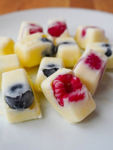 frozen yoghurt berry bites arranged on white plate close up on raspberry and blueberry