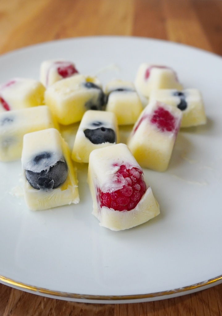 frozen yoghurt berry bites arranged on white plate close up on raspberry