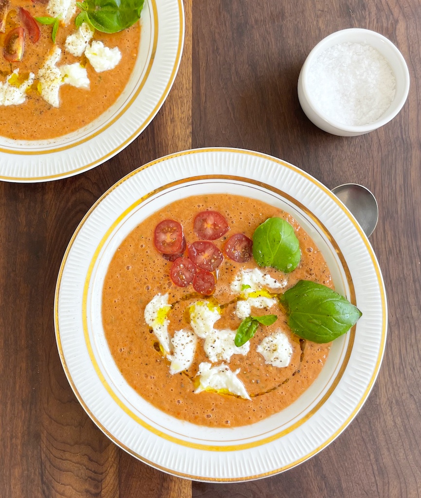 gazpacho with basil and mozzarella on two serving plates flat lay