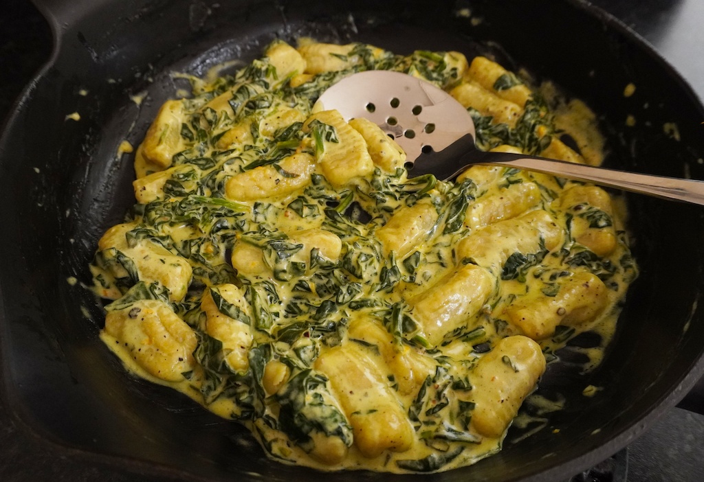 gnocchi with spinach and mascarpone in cast iron frying pan with serving spoon in close up
