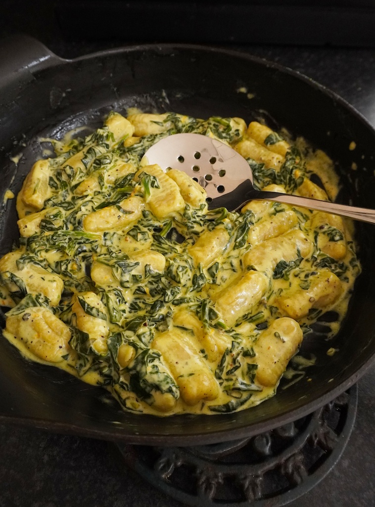 gnocchi with spinach and mascarpone in cast iron frying pan with serving spoon in