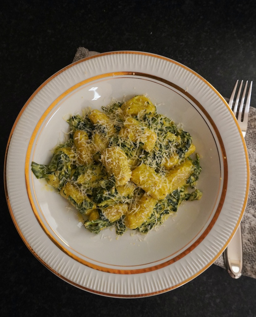 gnocchi with spinach and mascarpone in serving plate sprinkled with parmesan fork on right hand side of plate