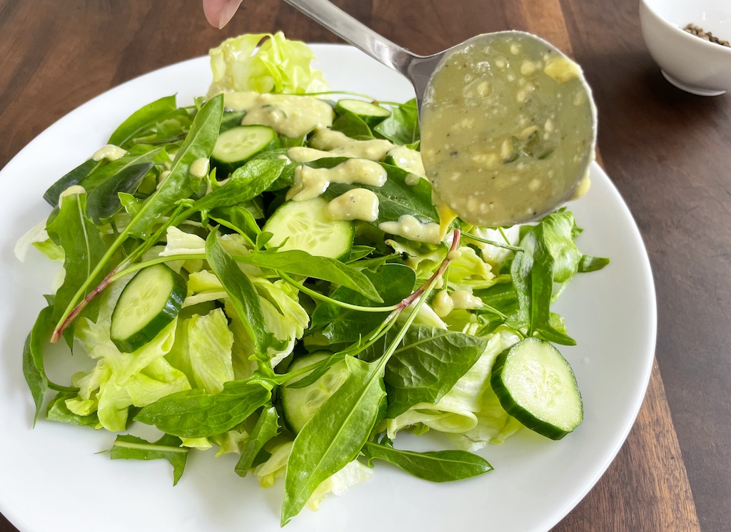 green salad with sorrel leaves and blue cheese dressing on a serving plate with a spoon pouring the dressing