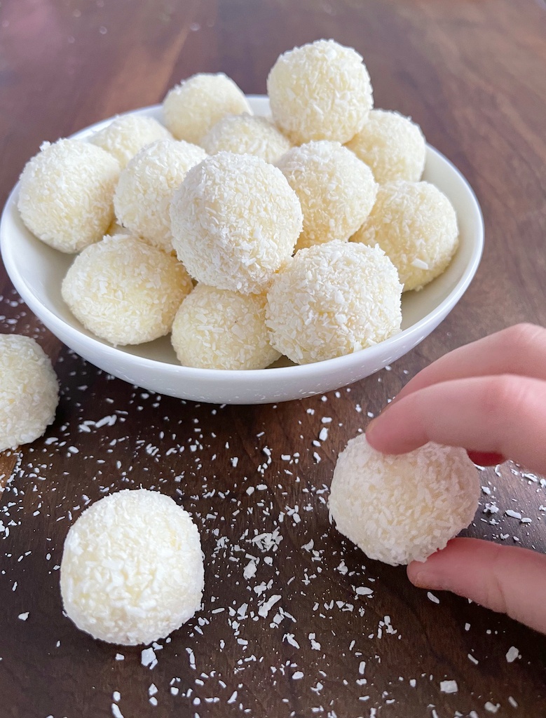 homemade coconut raffaello truffles in a bowl on the table with a child's hand picking one