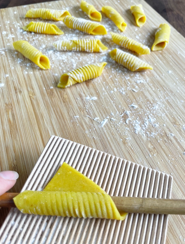 homemade garganelli pasta on wooden board with one pasta piece being made on gnocchi board
