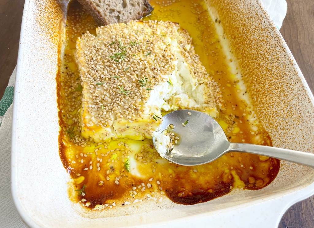 honey and lemon roasted feta in baking dish with a piece eaten with a spoon