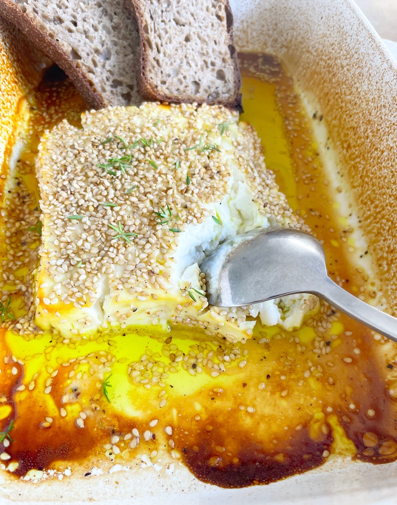 honey and lemon roasted feta in baking dish with bread and a spoon