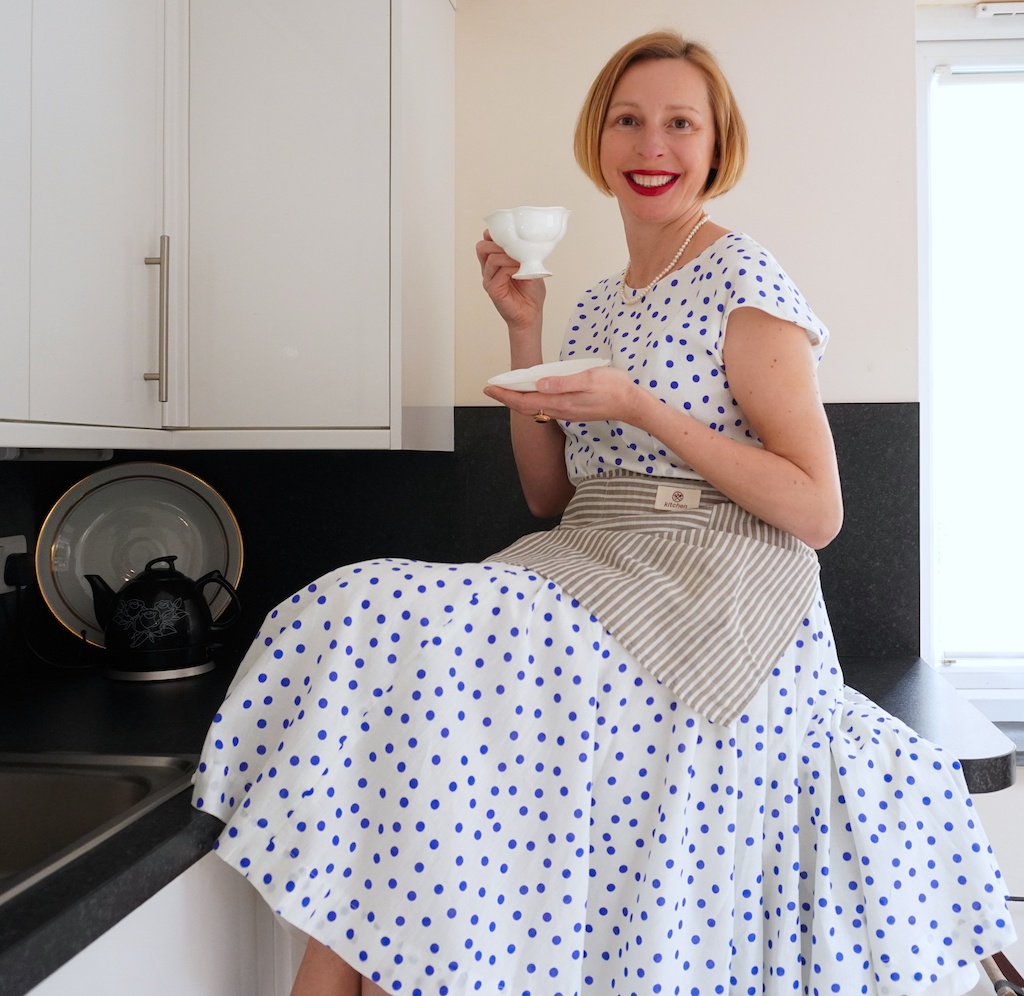 lady dressed in polka dot white and blue dress sitting on kitchen worktop with a cup and saucer in hands by 5 Element Cooking