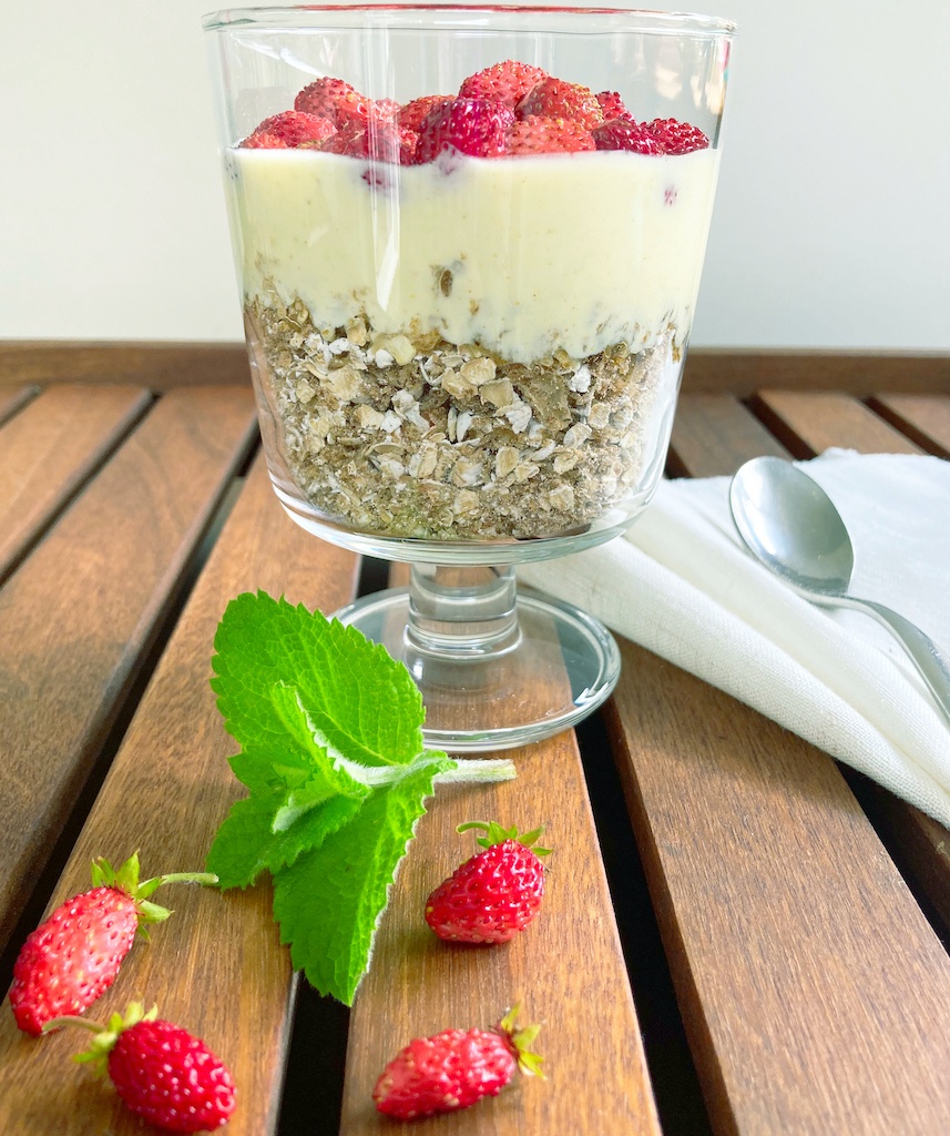 oats with spiced yoghurt and wild strawberries in a serving glass with a spoon and mint decoration