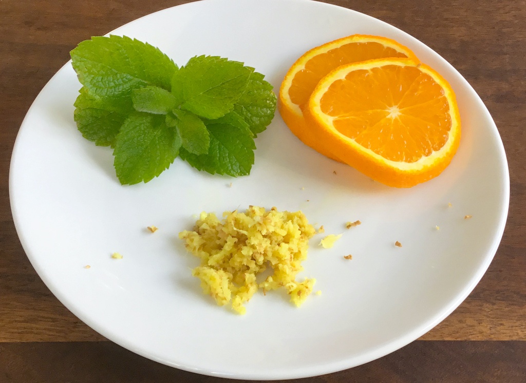 orange slices grated ginger and mint leaves on a white plate