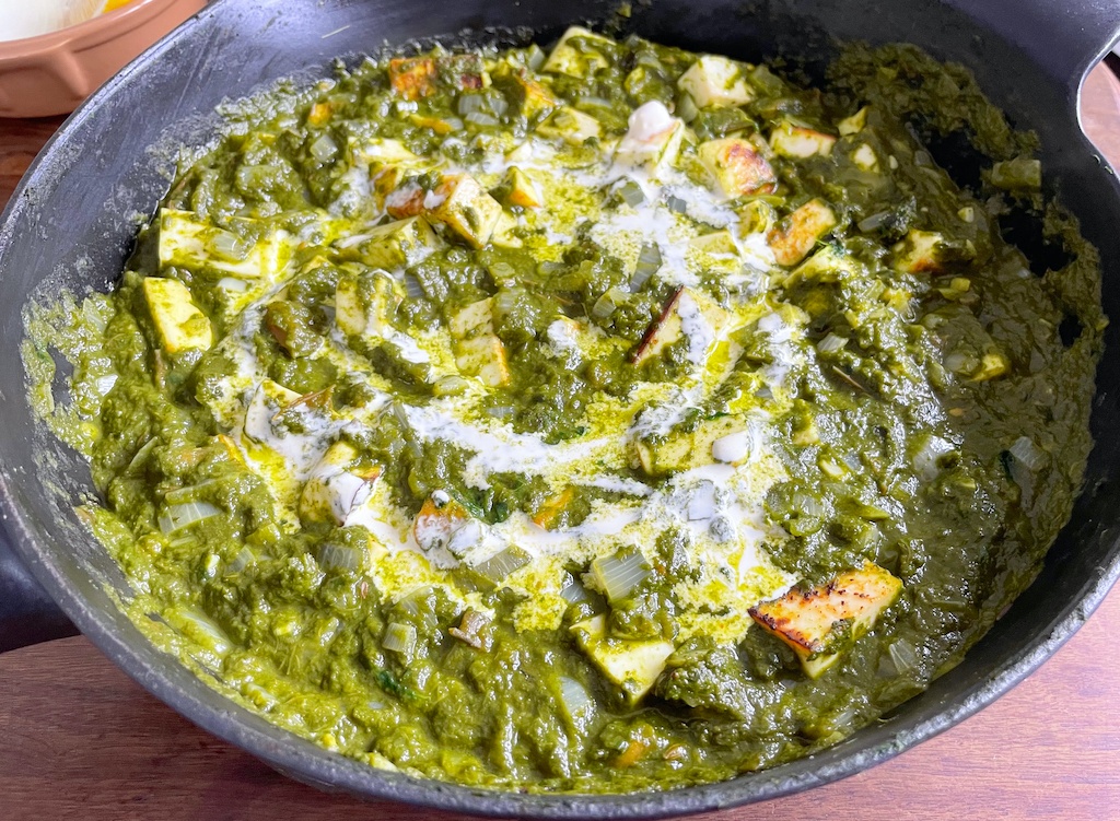 palak paneer in the frying pan with a dish in the background