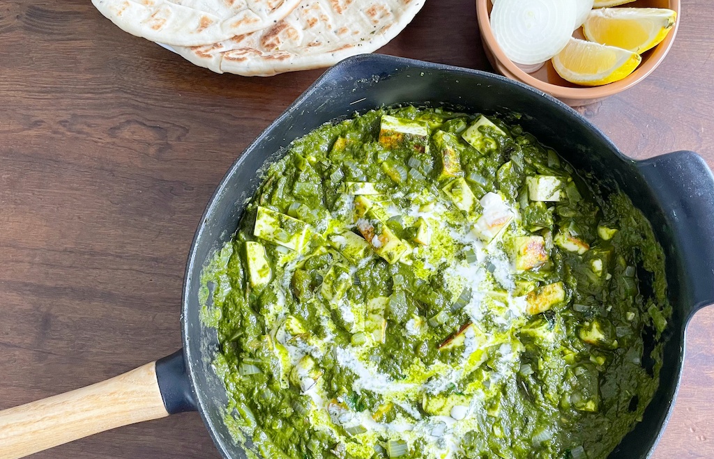 palak paneer in the frying pan with lemon and naan on the table