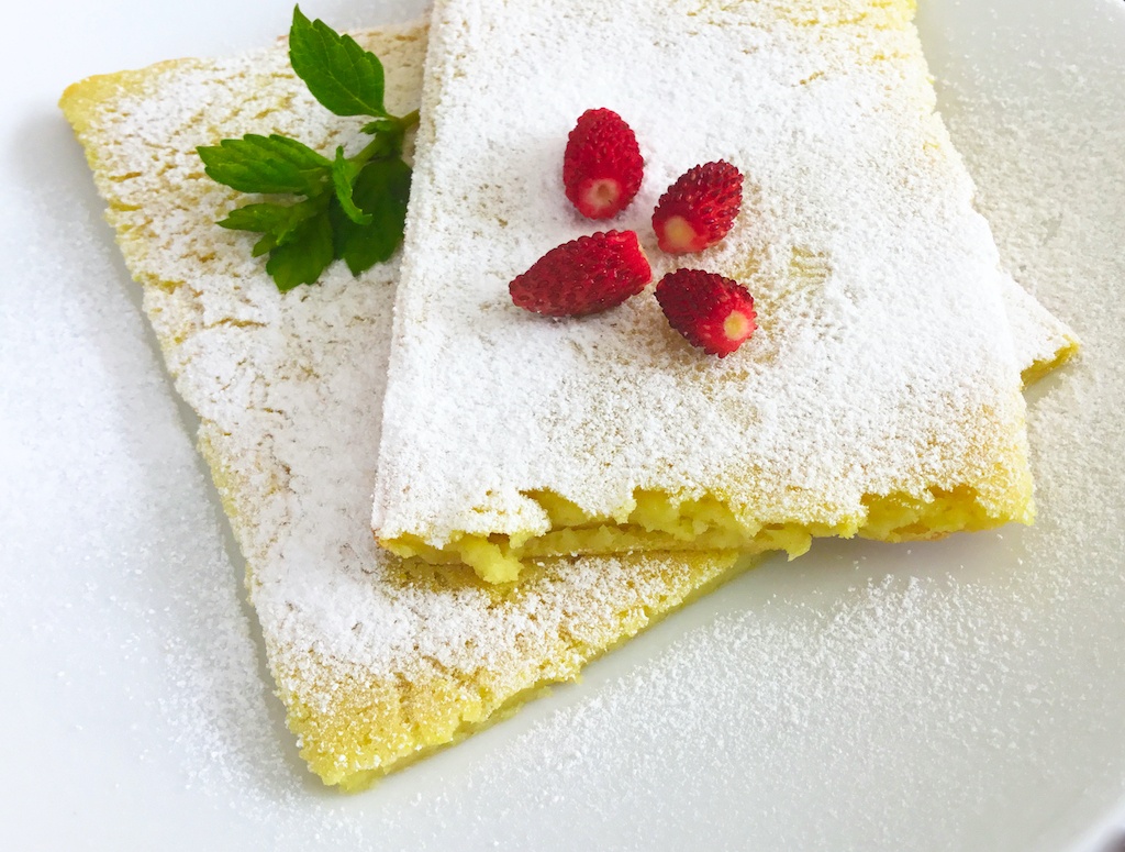 pannukakku - the pancake on the plate topped with icing sugar and wild strawberries