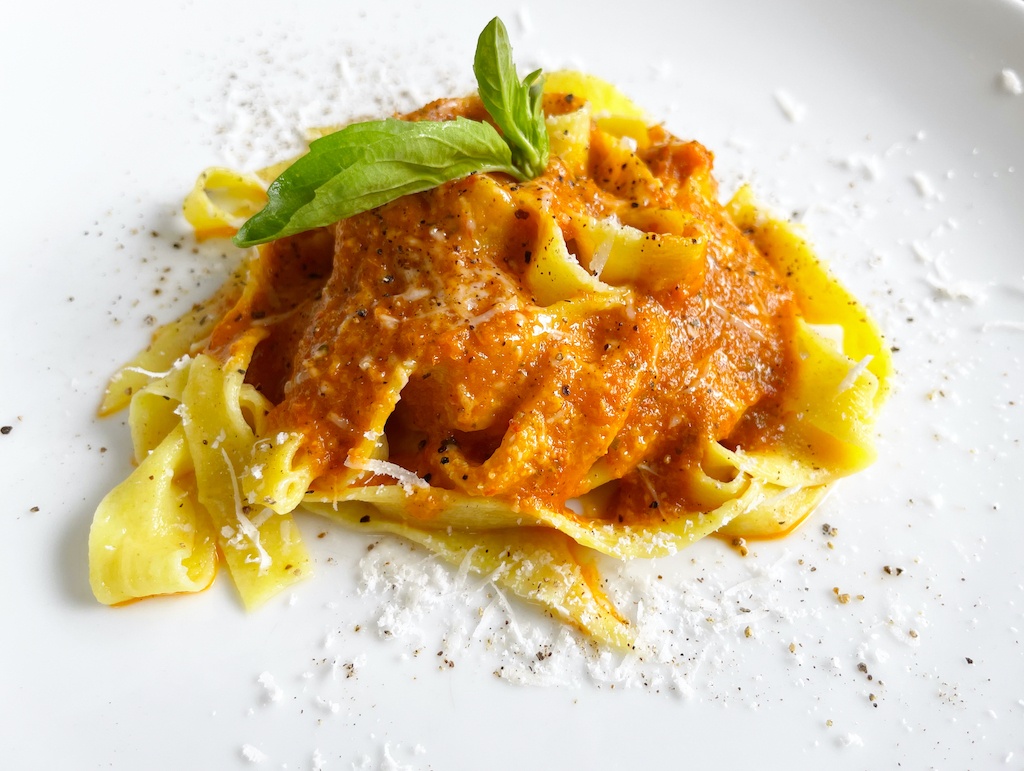 pappardelle with pepper and tomato sauce and a basil leaf on top