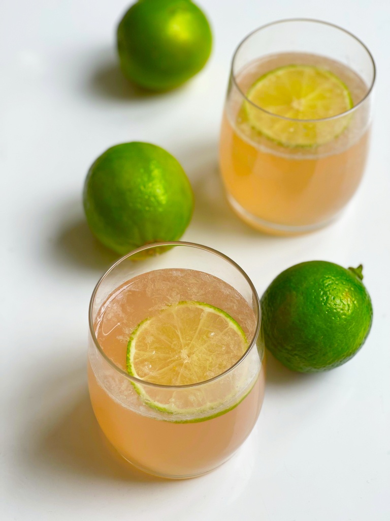 rhubarb tequila cocktail in two drinking glasses and limes around seen from the top