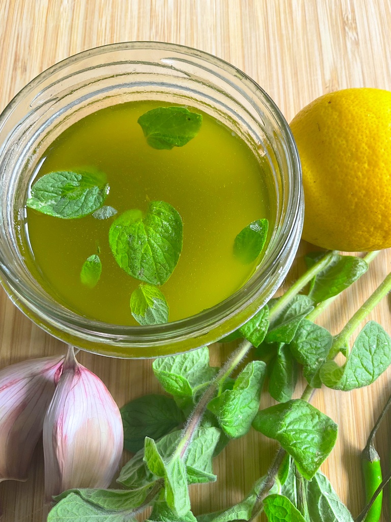 salmoriglio sauce in a jar with lemon, garlic and herbs on the side flat lay
