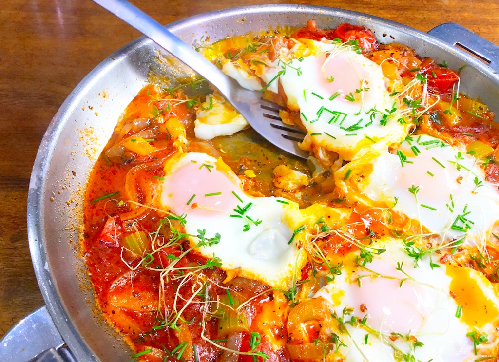 shakshouka in frying pan with a spoon taking a piece out