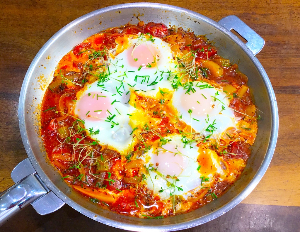 shakshouka with four eggs in frying pan on the table