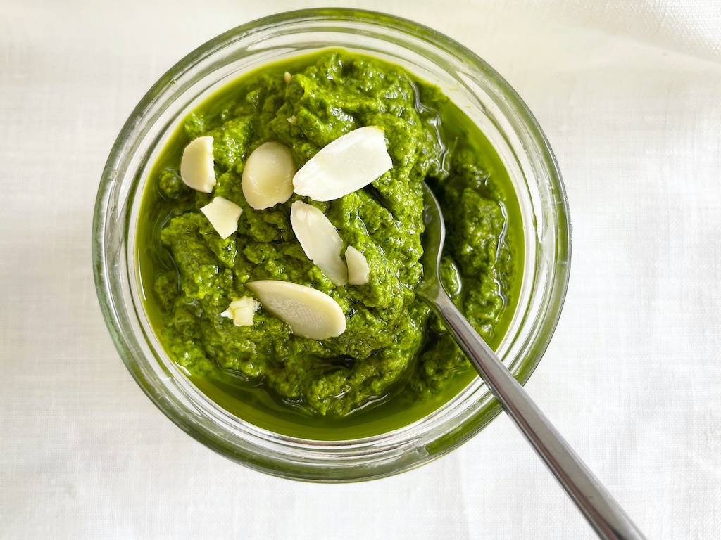 sorrel pesto in a jar with a spoon sprinkled with almond flakes flat lay