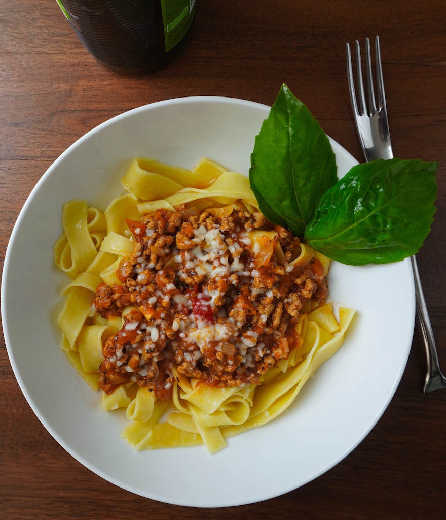 spaghetti bolognese in pasta bowl garnished with basil leaves fork on the table flat lay