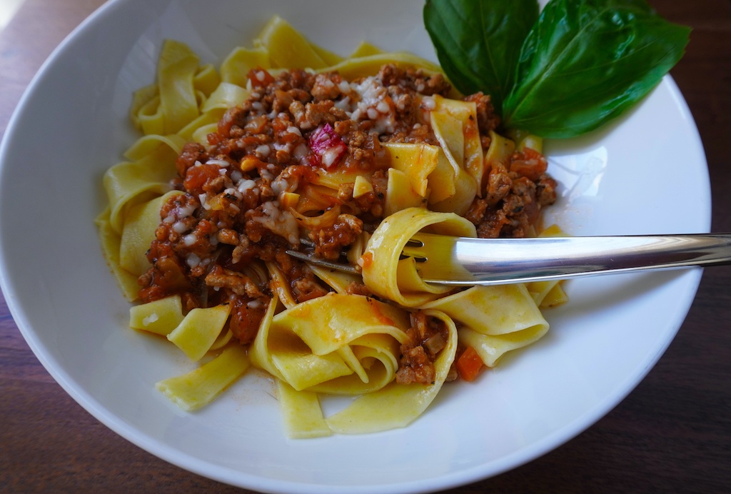spaghetti bolognese in pasta bowl garnished with basil leaves pasta piece around fork in bowl