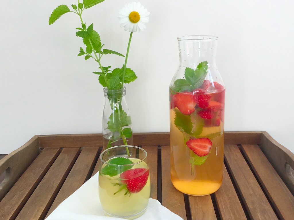 strawberry kombucha in a glass bottle with some in a glass and flowers in a glass pot