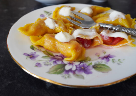 strawberry pierogi on serving plate garnished with soured cream and sugar one pierog cut open strawberries inside