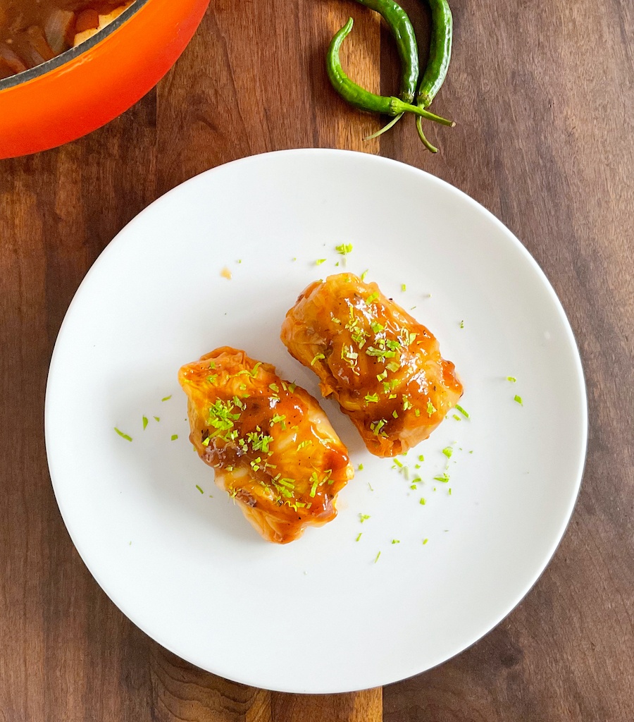 stuffed cabbage leaves or rolls on serving plate with a pan and green chillies on the side flat lay