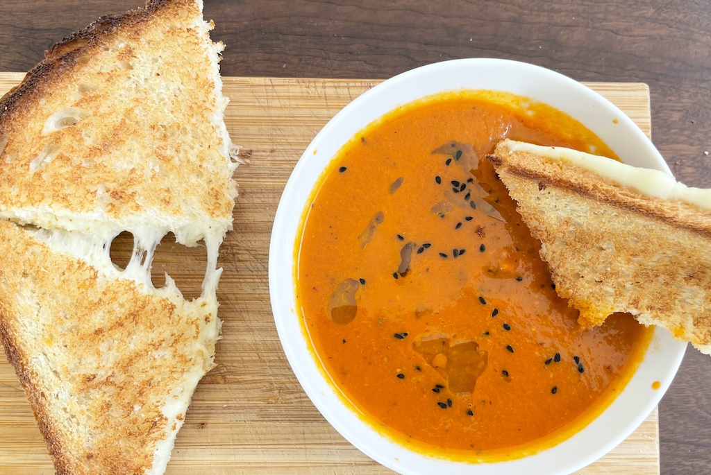 tomato harissa soup with a toast in the bowl and cheesy toasts on the side