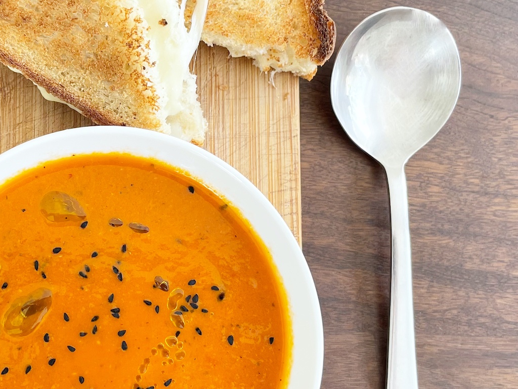 tomato harissa soup with some toast and a spoon on the side