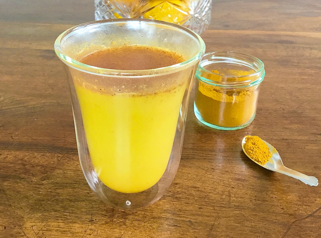turmeric latte in a glass with the powder in a jar