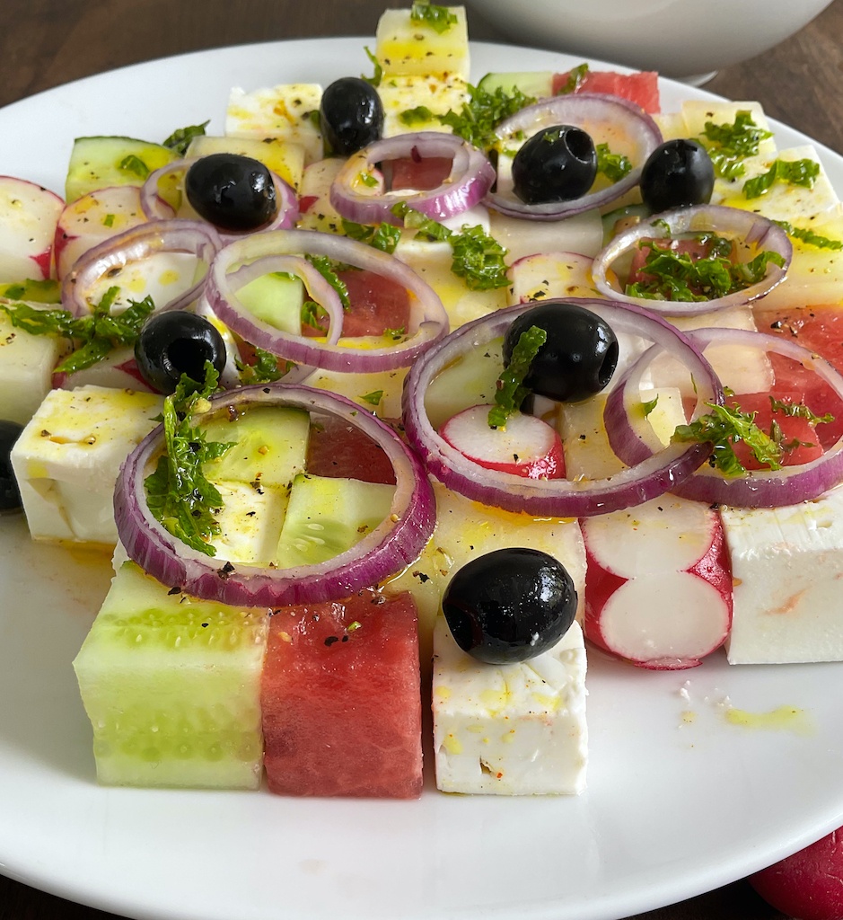 watermelon and feta tetris salad on the serving plate with onions, olives and dressing