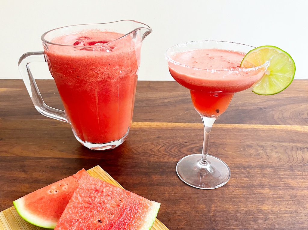 watermelon margarita in a drinking glass and a jug